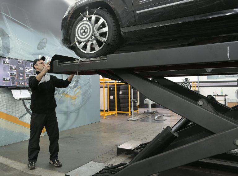 Mechanic carefully examining car on hydraulic lift in automotive workshop, ensuring safety and performance.
